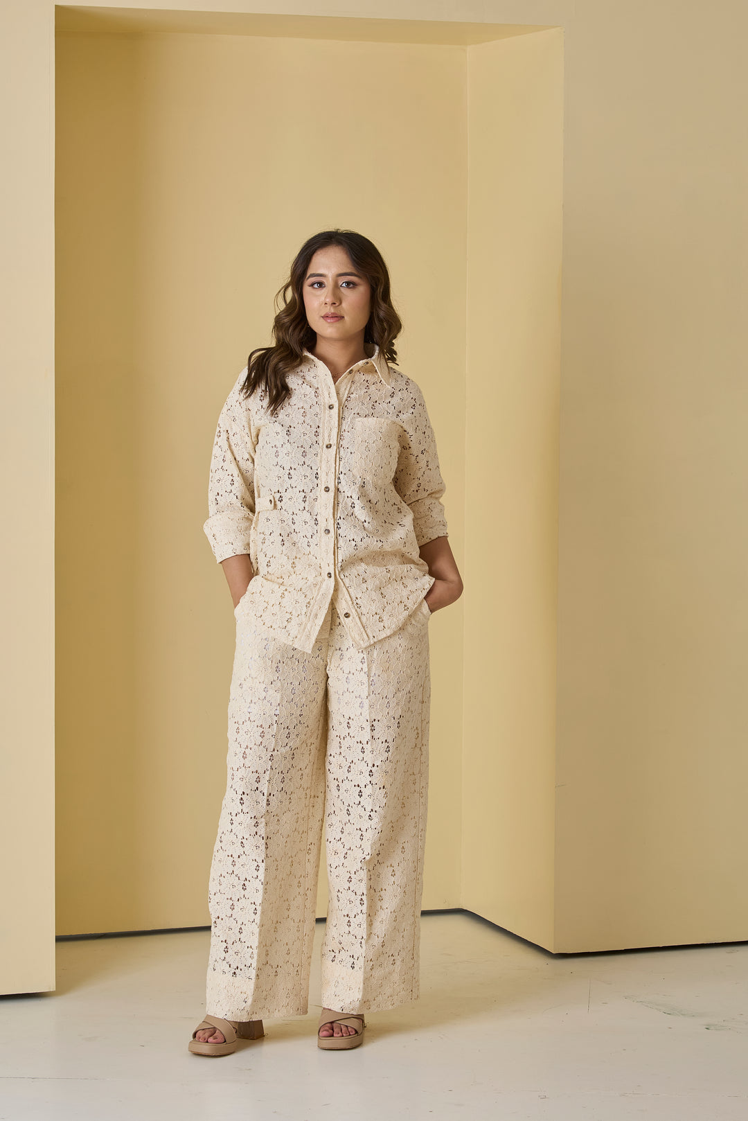 Woman wearing a beige patterned outfit standing in a minimalistic room with yellow walls.
