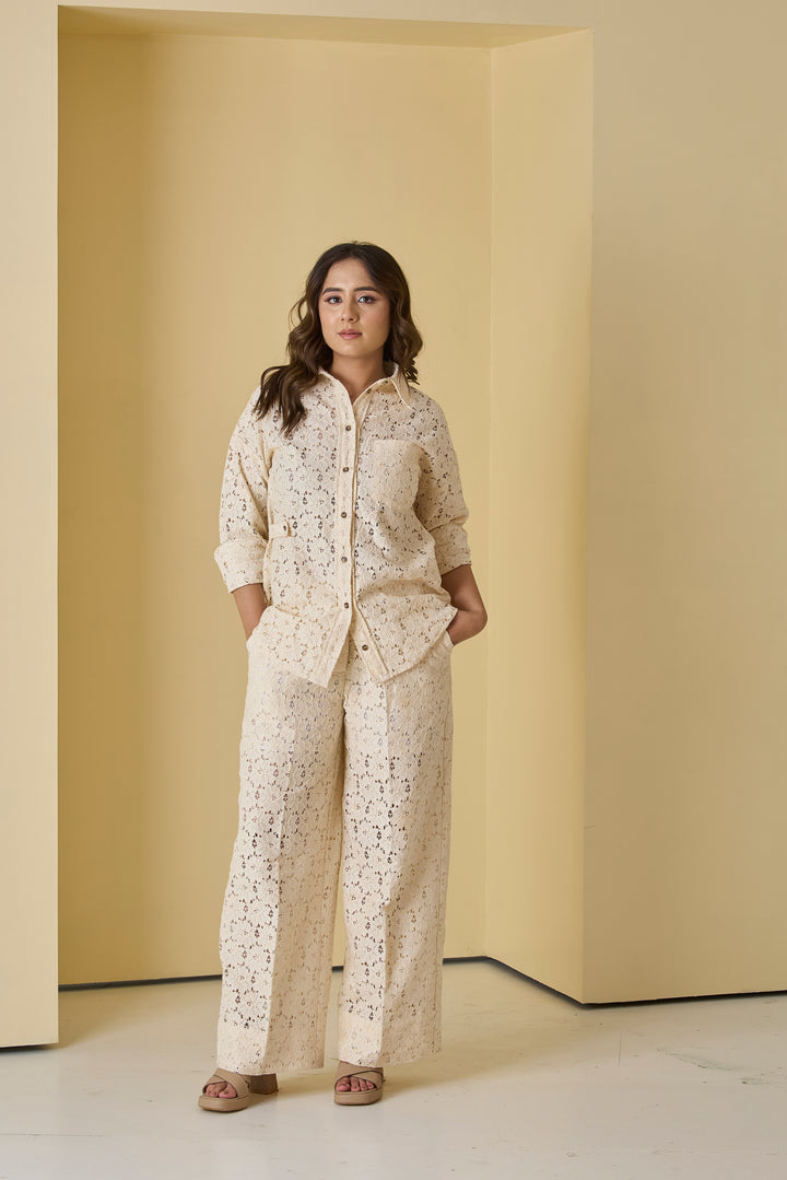Woman wearing a beige patterned outfit standing in a minimalistic room with yellow walls.