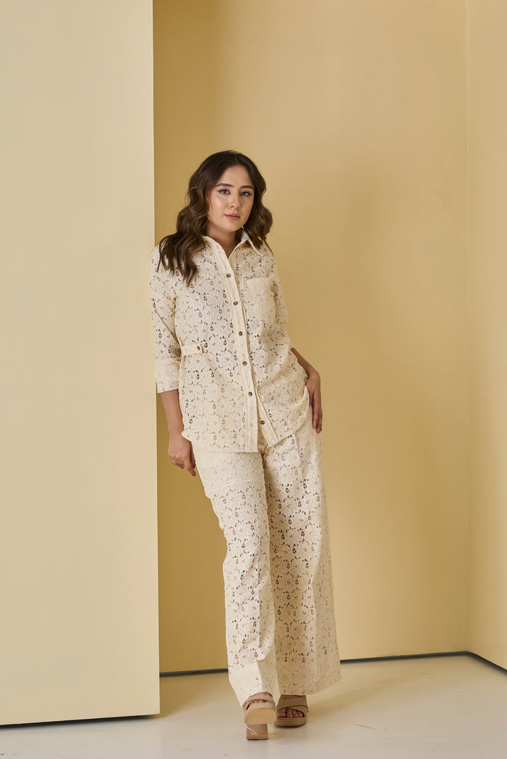 Woman wearing a beige lace outfit standing against a beige wall.