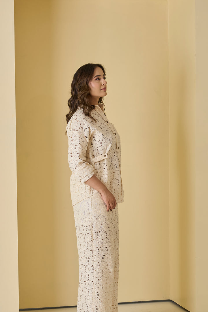 Woman wearing a white lace outfit standing against a beige wall