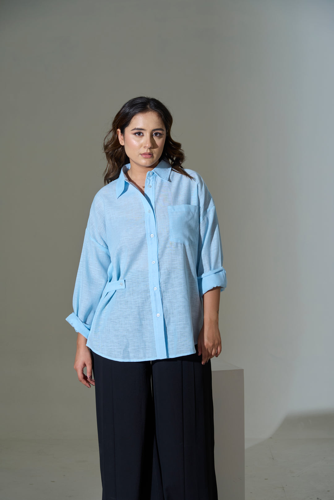Woman wearing a light blue shirt and dark pants against a plain background