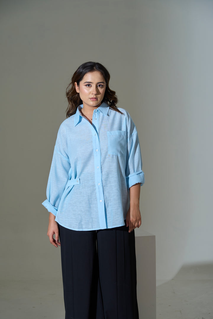 Woman wearing a light blue shirt and dark pants against a plain background
