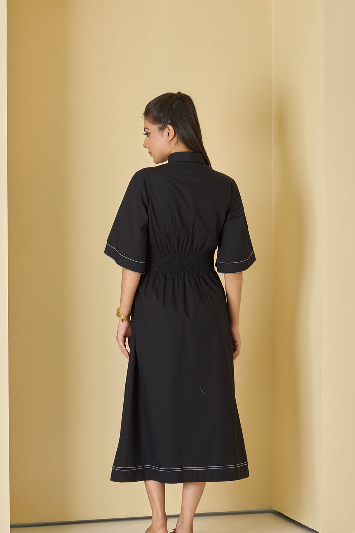 Woman wearing a black dress with white trim against a beige wall