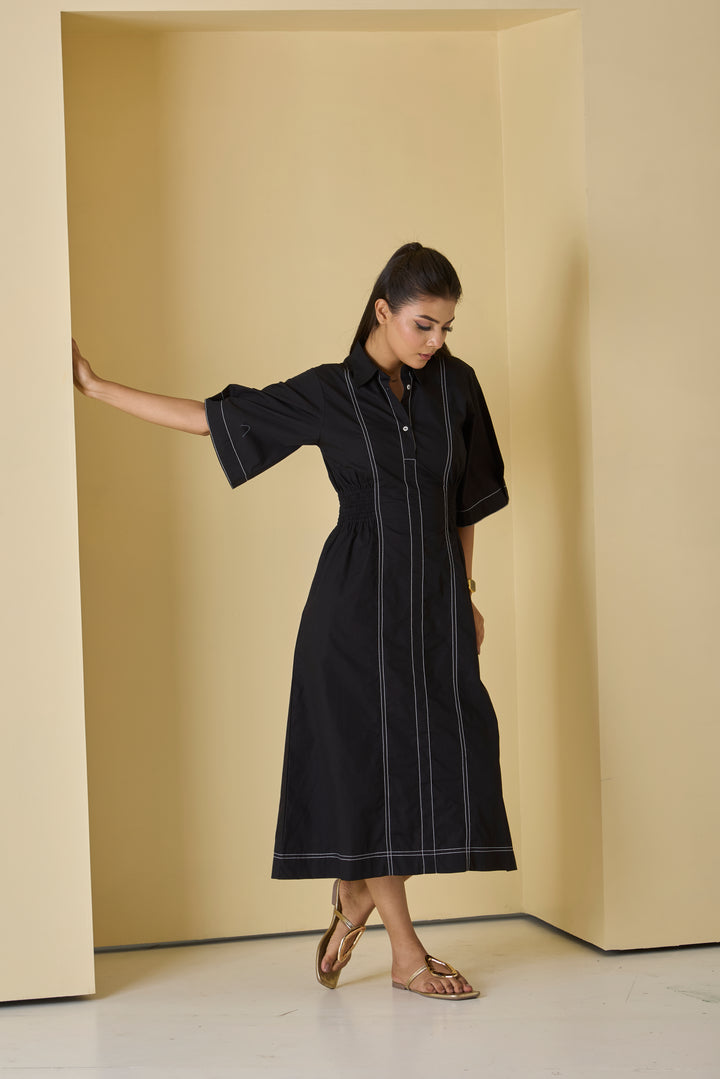 Woman wearing a black dress with white stripes in a minimalistic setting