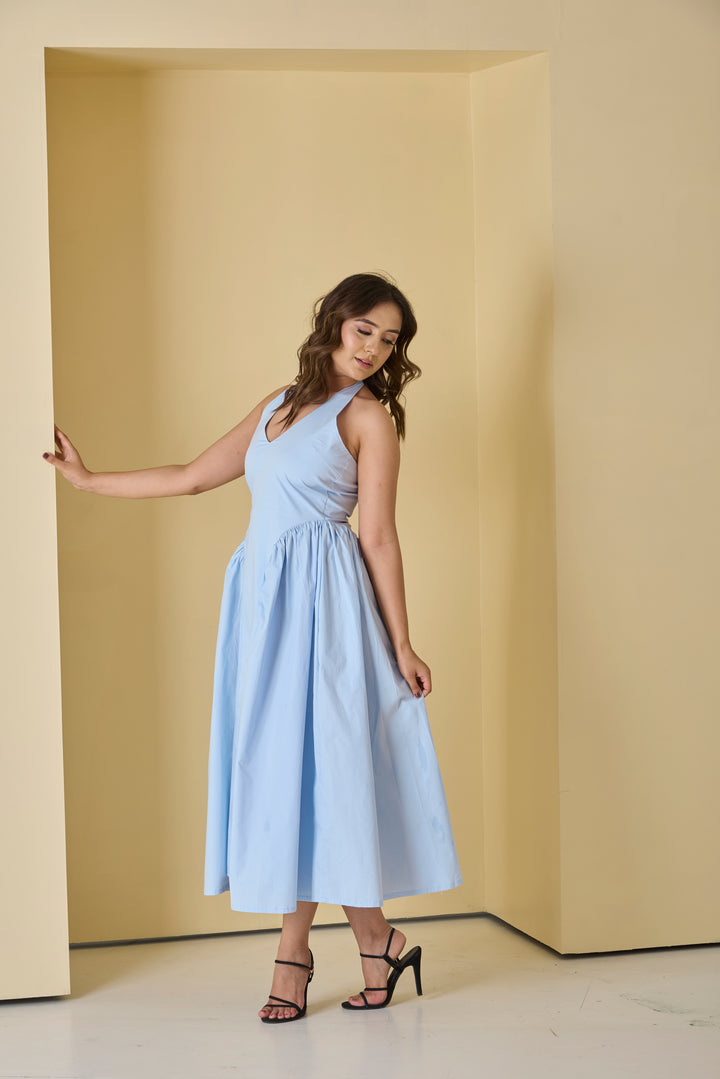Woman in a light blue dress standing in a minimalistic room with beige walls.