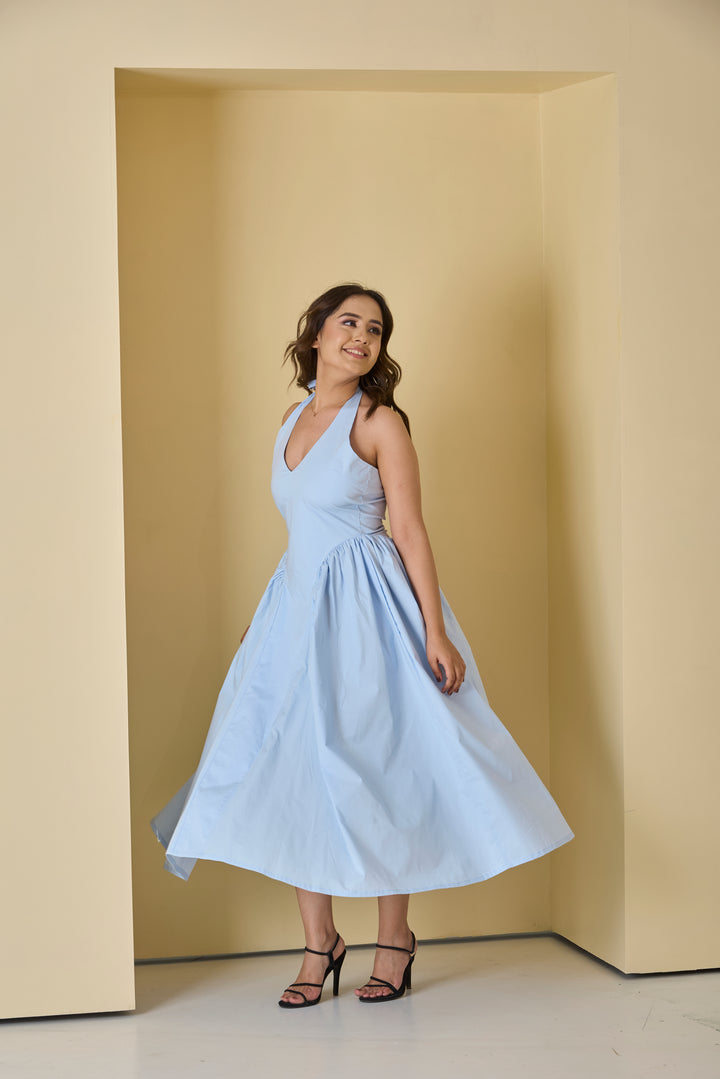 Woman in a light blue dress standing in a room with beige walls.