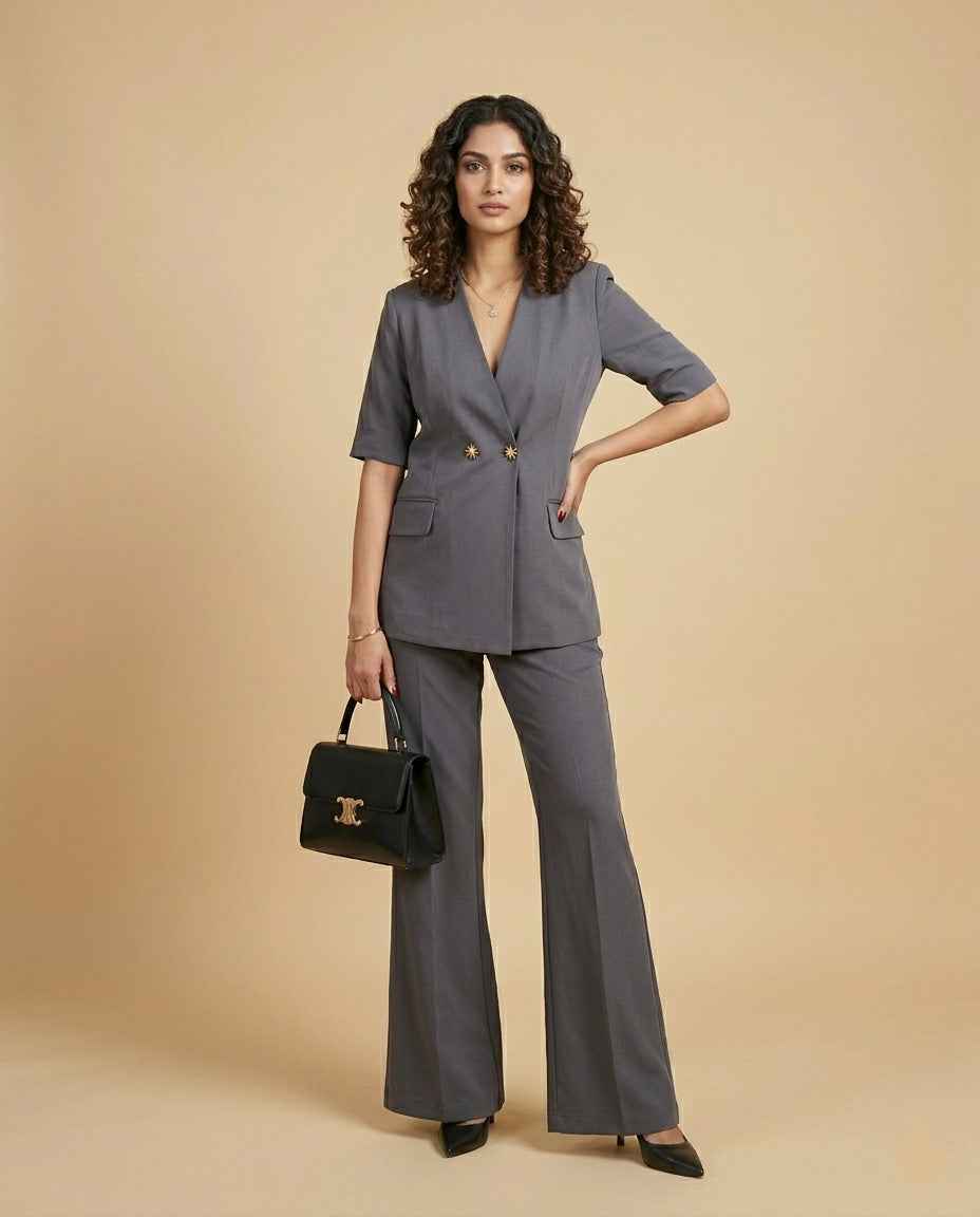 Woman wearing a charcoal grey suit standing against a plain 