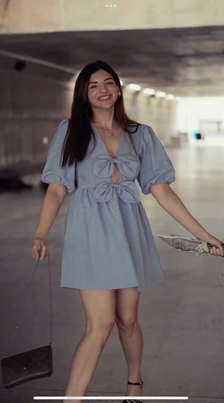 Risate blue mini dress with puff sleeves and front bow details worn by smiling woman