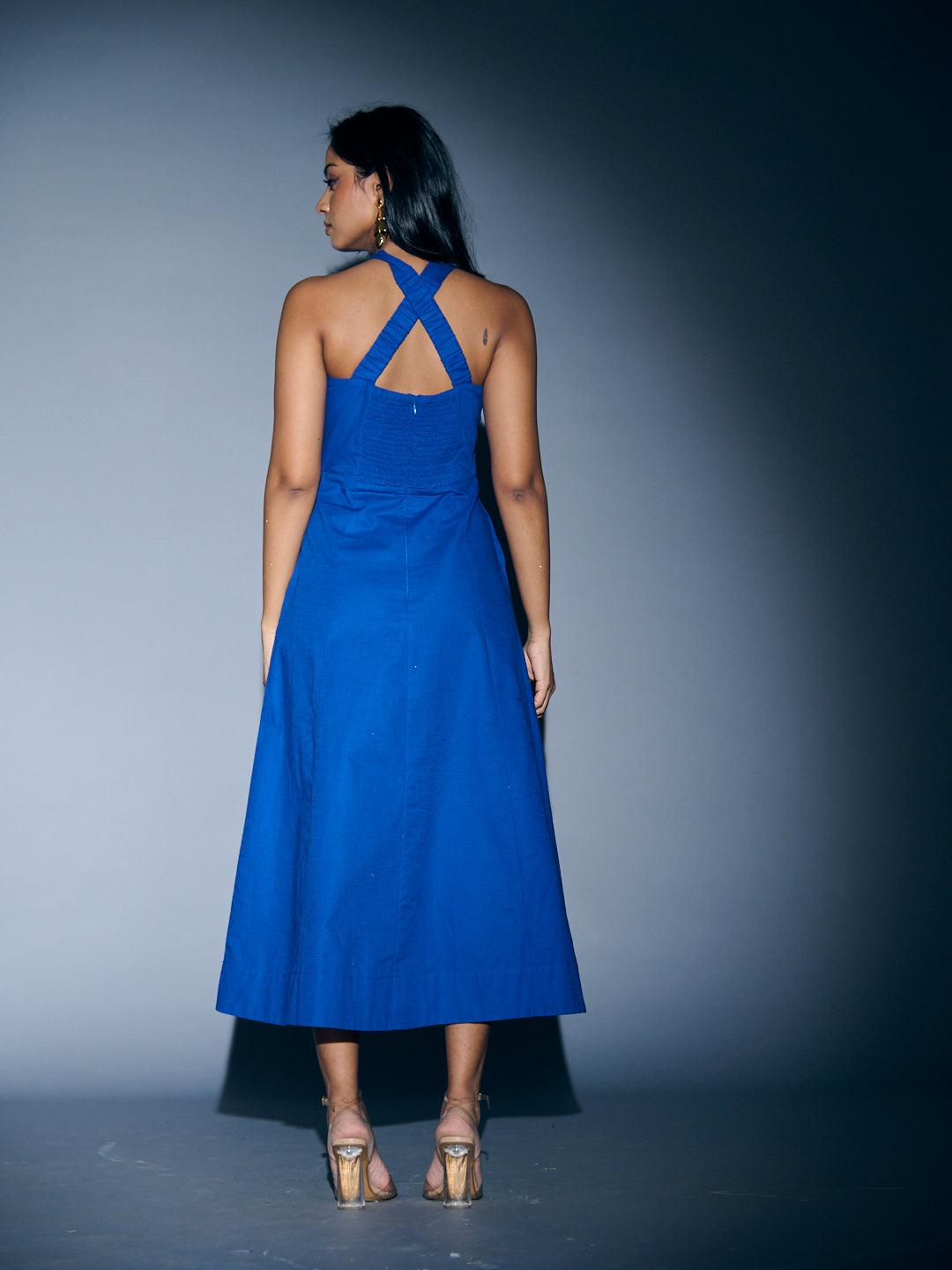 Back view of a blue Risate crossneck linen maxi dress with crisscross straps and a flowing silhouette