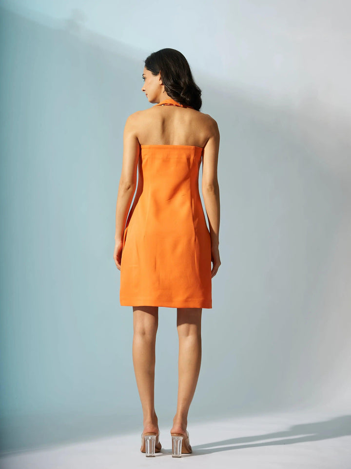 Back view of a woman wearing an orange halterneck crepe mini dress by Risate against a light background