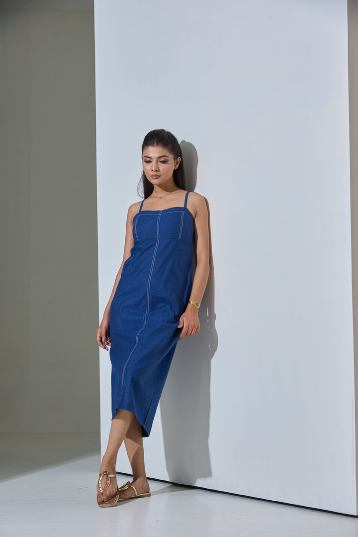 Woman wearing a blue dress standing against a white wall.