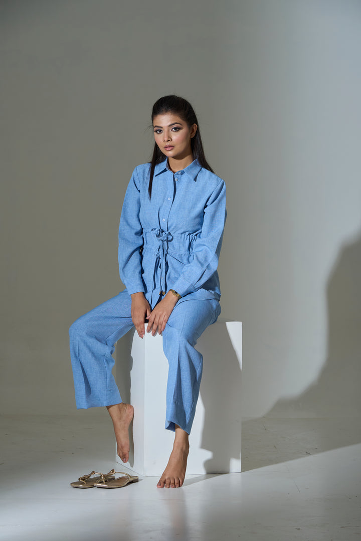 Woman in a blue outfit sitting on a white block against a plain background