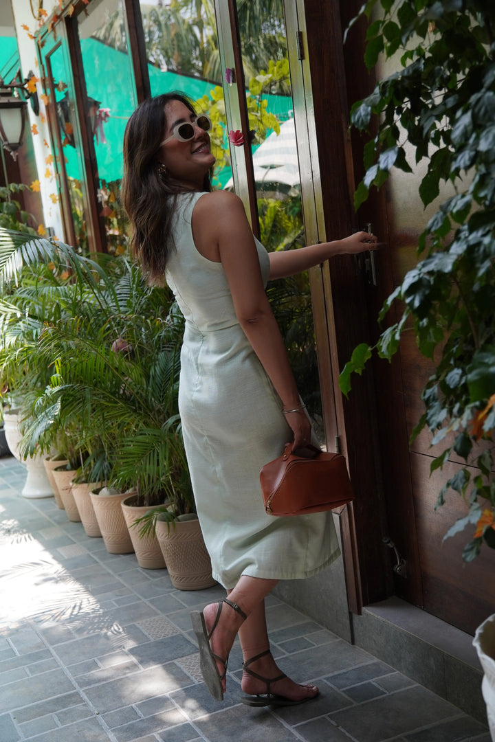 Woman wearing a sage cut out dress, styled with sunglasses and holding a brown handbag