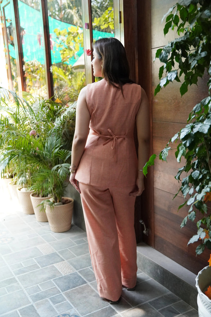 Woman wearing Risate Terra Set co-ord set in soft terracotta color standing by a window near plants