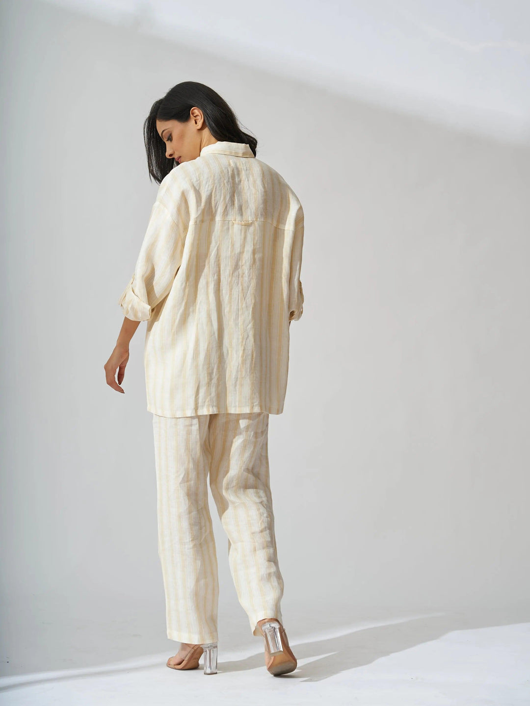 Back view of a woman wearing a yellow stripes linen coord set for women, featuring a loose-fitting shirt and trousers